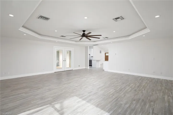 Spacious open-plan room featuring light wood-look flooring, white walls, and a tray ceiling with recessed lighting and a ceiling fan