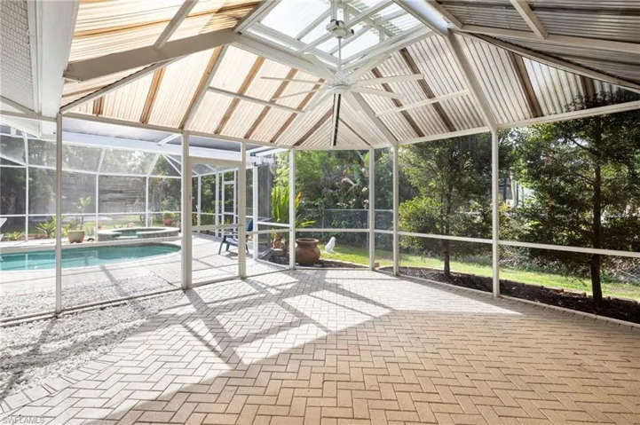 Expansive screened-in lanai with a vaulted ceiling and a ceiling fan, featuring a paved patio and views of the swimming pool and surrounding greenery