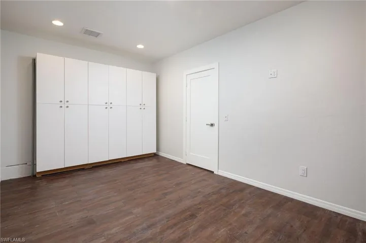 This bonus room features recessed lighting, extensive white cabinetry with silver hardware, and dark wood-style flooring