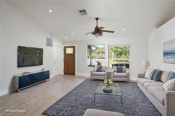 The living area features light-toned luxury vinyl flooring, a brand new wooden entry door with a glass insert, and a ceiling fan with integrated lighting