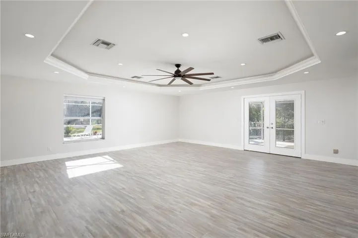 The expansive room features light-colored wood-style flooring, a tray ceiling with recessed lighting and a ceiling fan, and French doors providing access to the pool and spa.