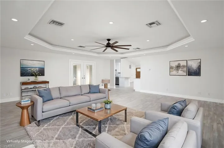 The living area features a tray ceiling with recessed lighting, ceiling fan, light-toned luxury vinyl flooring, white walls and new baseboards.