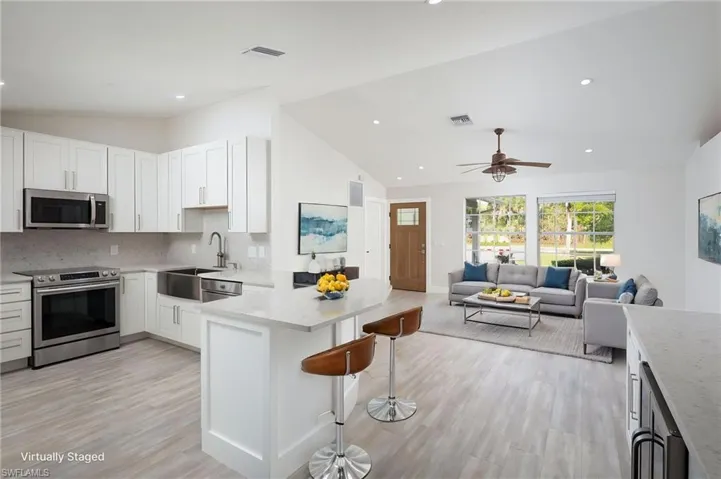 Open concept kitchen and living area featuring a vaulted ceiling with recessed lighting, a modern ceiling fan, and light wood-look flooring