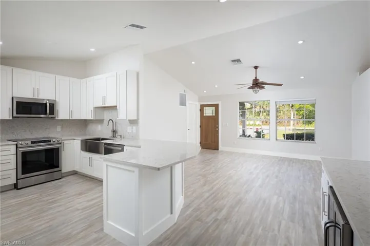 The remodeled kitchen features white cabinetry, stainless steel appliances including a wine cooler, and a farmhouse-style sink, complemented by light-colored quartz countertops