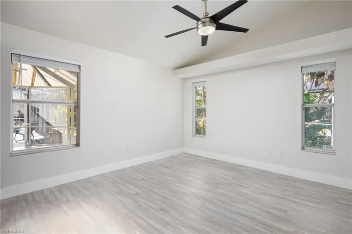 The primary bedroom features light-colored luxury vinyl flooring, new baseboards and trim, new interior door, white walls, and a vaulted ceiling with a modern ceiling fan.