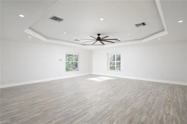 Spacious family room featuring light-toned luxury vinyl flooring, white walls, new baseboards and a tray ceiling with recessed lighting and a ceiling fan