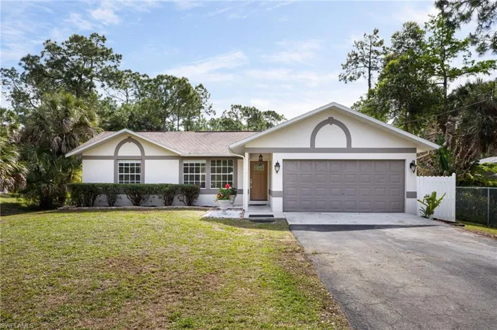 The property features a well-maintained lawn, an attached garage, a paved driveway, and mature landscaping