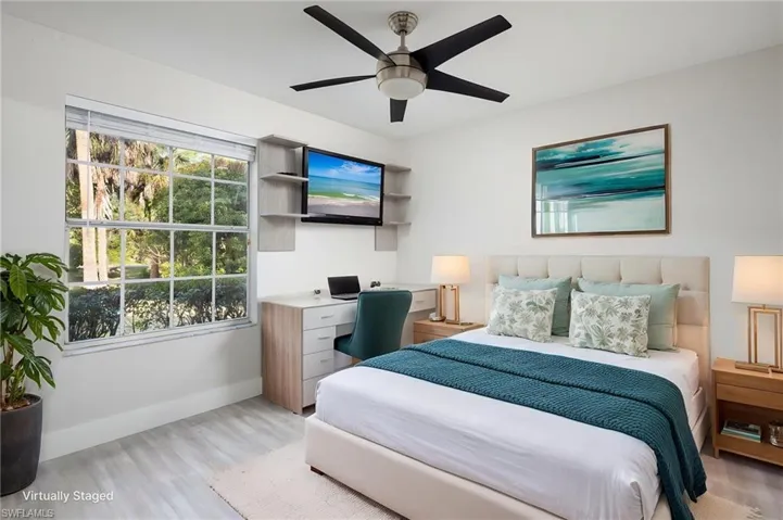 This room features a window providing views of greenery, light-toned flooring, new baseboard, trim, interior door, a ceiling fan, and a built-in desk with shelving