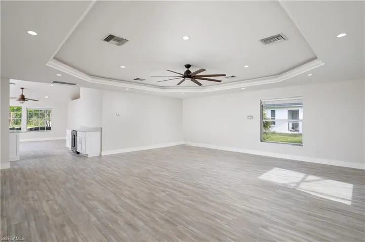 Expansive living area featuring light-toned luxury vinyl flooring, new baseboard & trim, a tray ceiling with recessed lighting, and a ceiling fan