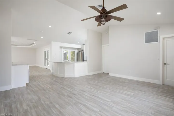 Spacious living area featuring light-toned flooring, a ceiling fan with light fixture, and recessed lighting