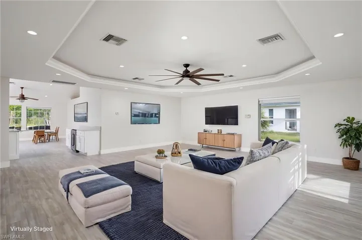 Expansive living area featuring light-toned luxury vinyl flooring, new baseboard & trim, a tray ceiling with recessed lighting, and a ceiling fan. Interior of entire home freshly painted.