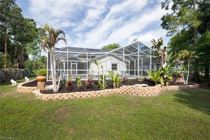 The property features a screened-in patio enclosure, a manicured lawn, and a tiered garden bed with various plantings