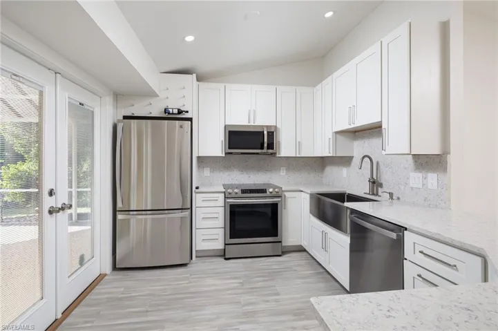 Well-appointed kitchen featuring white cabinetry, light-colored quartz countertops, and stainless steel appliances, french doors with access to the covered lanai, pool & spa area.