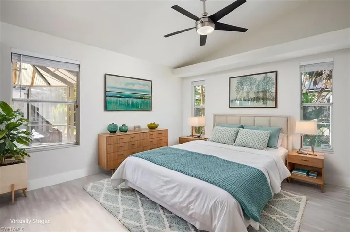 The primary bedroom features light-colored luxury vinyl flooring, new baseboards and trim, new interior door, white walls, and a vaulted ceiling with a modern ceiling fan