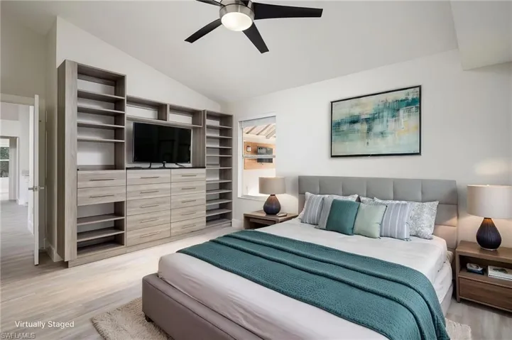 This spacious primary bedroom features vaulted ceilings, wooden storage/shelving, new baseboard, trim and interior door, ceiling fan, and light wood tone flooring