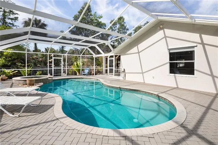 The property features a screened pool and spa area, complemented by a paver patio and views of lush greenery