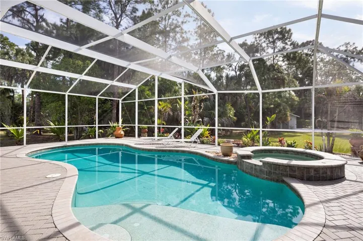 The property features a screened-in heated swimming pool and an integrated hot tub, surrounded by a paved patio area