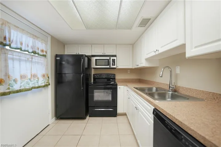 Kitchen featuring black appliances, light countertops, light tile patterned floors, and white cabinetry