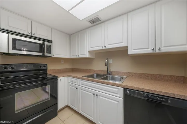 Kitchen with black appliances, white cabinets, light tile patterned floors, and light countertops