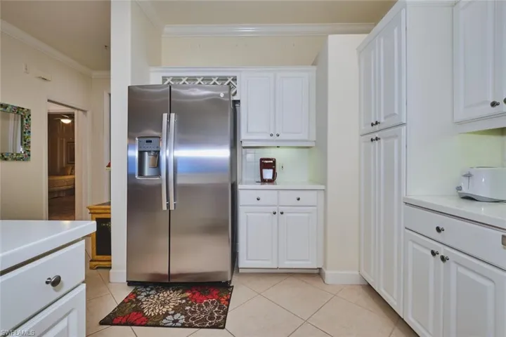 Kitchen featuring stainless steel refrigerator with ice dispenser, white cabinets, light tile patterned floors, crown molding, and backsplash