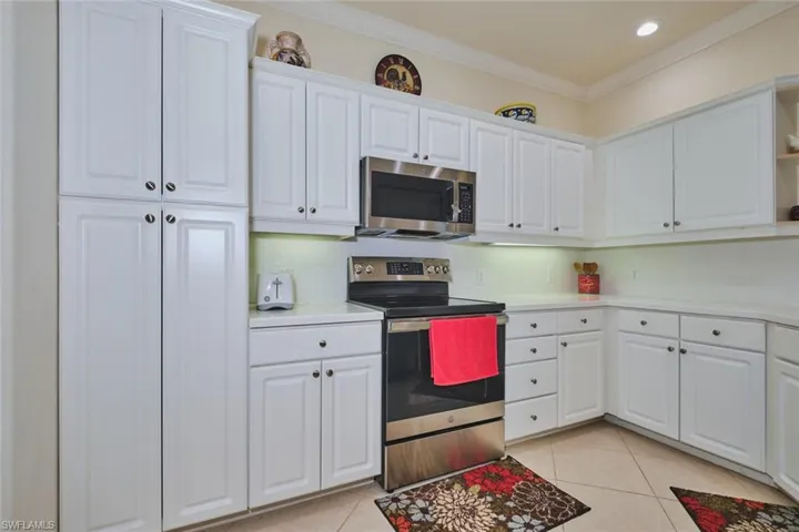 Kitchen with appliances with stainless steel finishes, white cabinets, light tile patterned floors, decorative backsplash, and light countertops