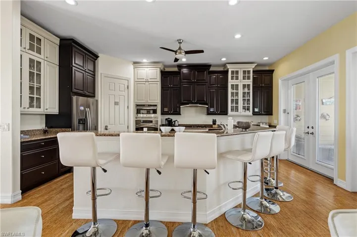 Kitchen featuring light wood-style flooring, glass insert cabinets, a ceiling fan, a breakfast bar, and appliances with stainless steel finishes
