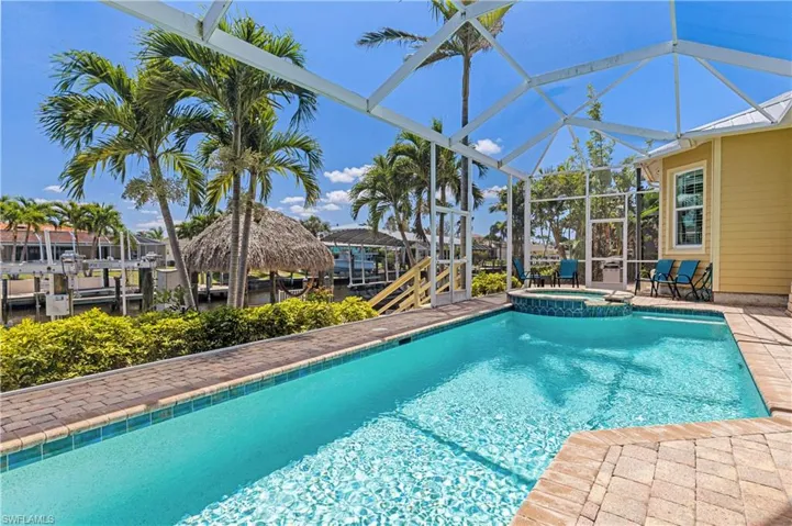 View of swimming pool with a tiki-hut, patio area, heated pool/ hot tub, andscreened in lanai