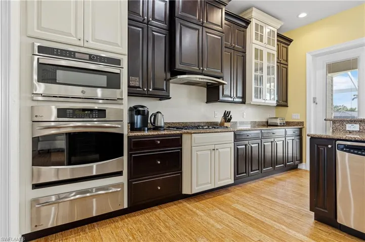 Kitchen featuring light wood-style flooring, a warming drawer, glass insert cabinets, under cabinet range hood, and appliances with stainless steel finishes