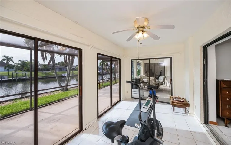 Workout room with a water view, a ceiling fan, and light tile patterned flooring