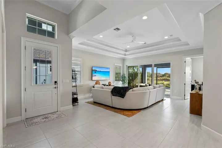Living room features ceiling fan, recessed lighting, light tile patterned flooring, and a tray ceiling