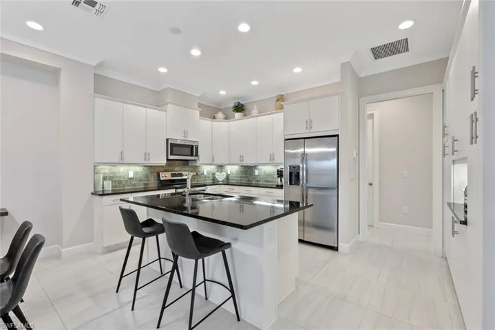Kitchen featuring stainless steel appliances, white cabinetry, a center island with sink, and a kitchen breakfast bar