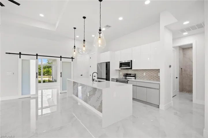Contemporary kitchen featuring a large island with a waterfall countertop, sleek cabinetry, and pendant lighting