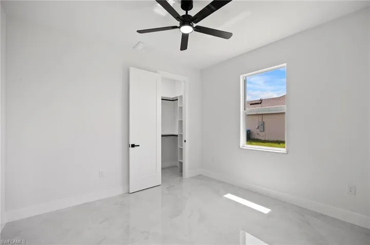 Bright interior space featuring a matte black ceiling fan, white paneled door with black hardware, and an open closet with built-in shelving