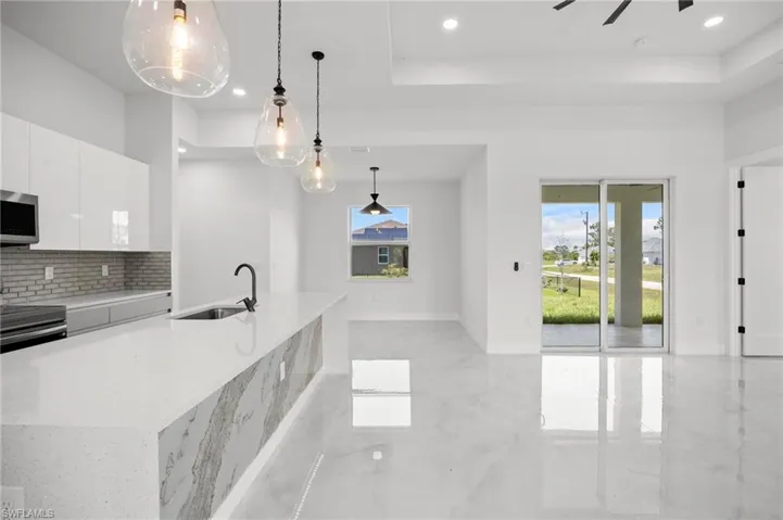 Modern open-concept living space featuring high-gloss tile flooring, a kitchen island with stone waterfall countertop, minimalist white cabinetry, and stainless steel appliances