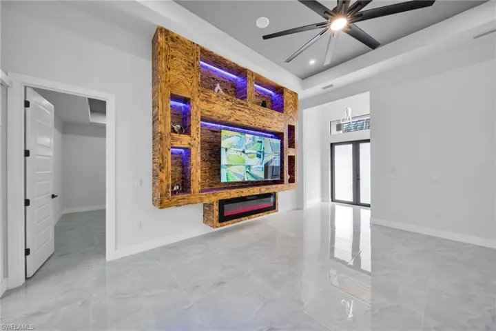 Unfurnished living room with a glass covered fireplace, a ceiling fan, light marble finish floors, and a towering ceiling