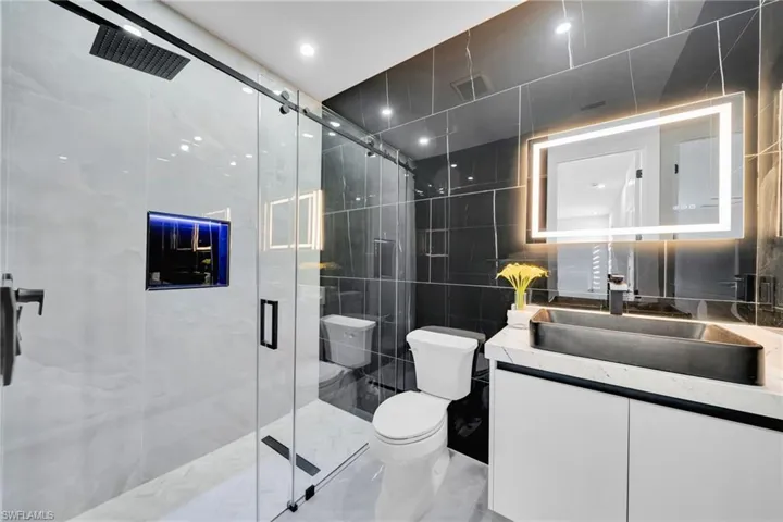 Full bath featuring tile walls, vanity, a stall shower, and recessed lighting