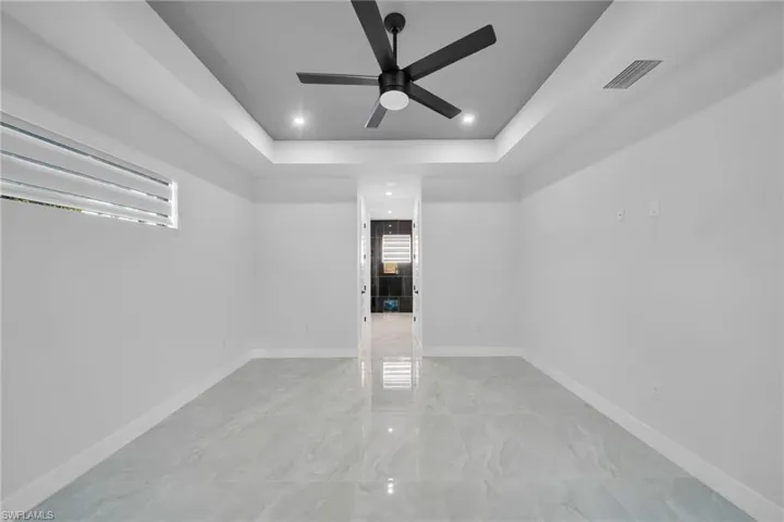Empty room featuring a tray ceiling, a ceiling fan, recessed lighting, and light marble finish flooring