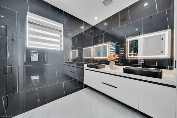 Bathroom featuring radiator, double vanity, tile walls, and recessed lighting