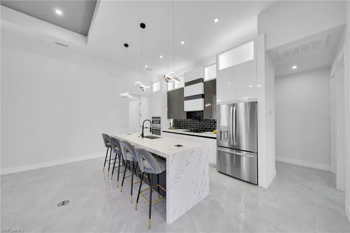 Kitchen featuring modern cabinets, pendant lighting, stainless steel refrigerator with ice dispenser, a center island with sink, and white cabinetry