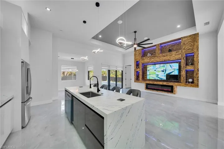 Kitchen featuring white cabinetry, a glass covered fireplace, decorative light fixtures, an island with sink, and a raised ceiling