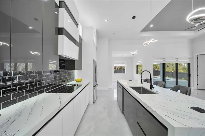 Kitchen featuring modern cabinets, white cabinetry, decorative light fixtures, light stone counters, and recessed lighting