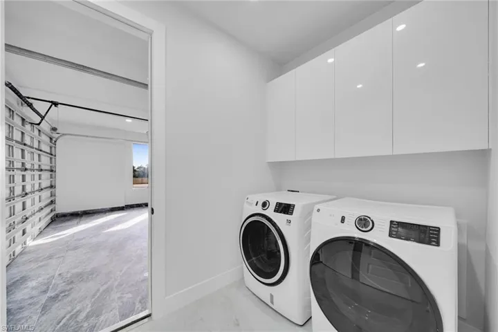 Laundry room with washer and dryer, light marble finish floors, recessed lighting, cabinet space, and a garage