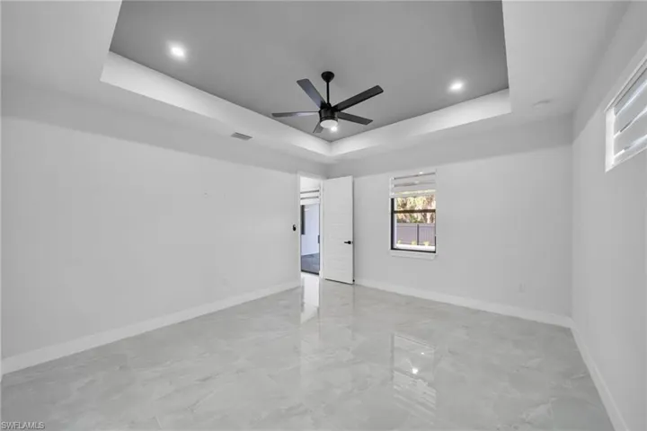 Spare room with a ceiling fan, light marble finish floors, a raised ceiling, and recessed lighting