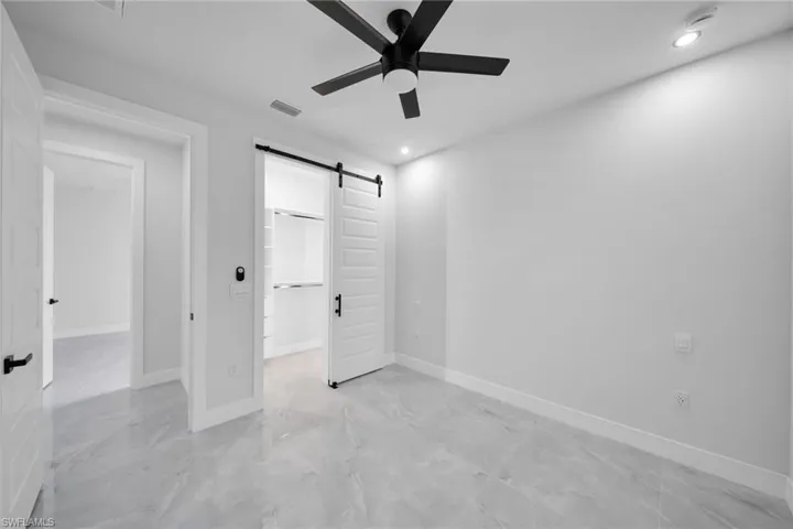 Unfurnished bedroom featuring a barn door, a walk in closet, a ceiling fan, and recessed lighting