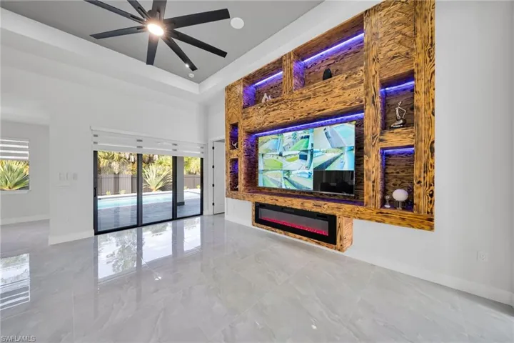 Unfurnished living room with a glass covered fireplace, a ceiling fan, marble tiled flooring, a high ceiling, and a raised ceiling