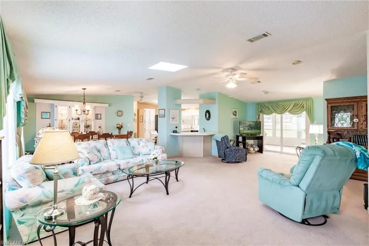 Living room with light carpet, a skylight, a textured ceiling, and ceiling fan with notable chandelier