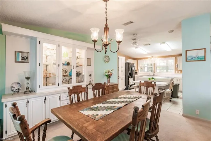 Tiled dining area with ceiling fan with notable chandelier, sink, a textured ceiling, and vaulted ceiling