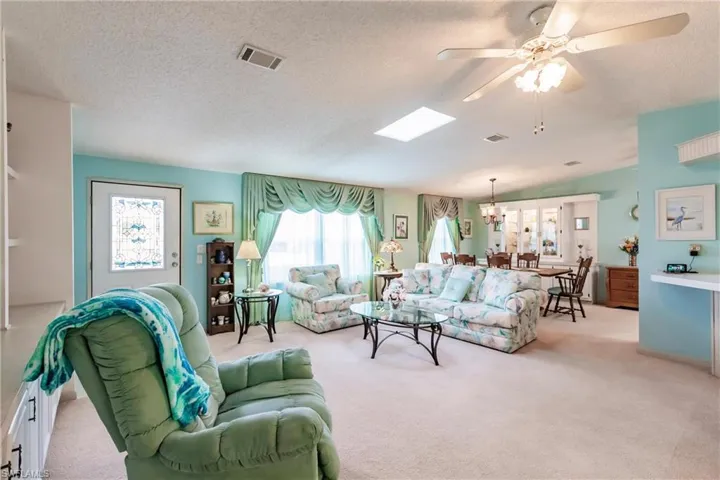 Living room featuring light carpet, a textured ceiling, and ceiling fan with notable chandelier