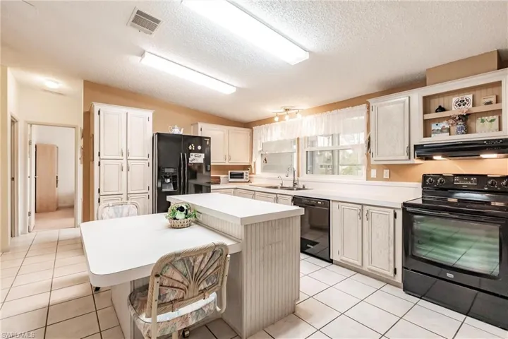 Kitchen featuring black appliances, lofted ceiling, a center island, sink, and light tile patterned floors