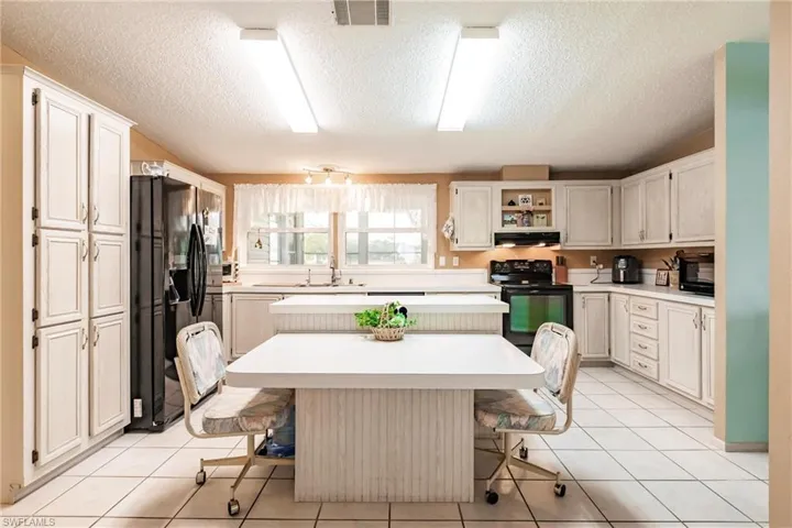 Kitchen with black appliances, a center island, sink, light tile patterned floors, and a breakfast bar area